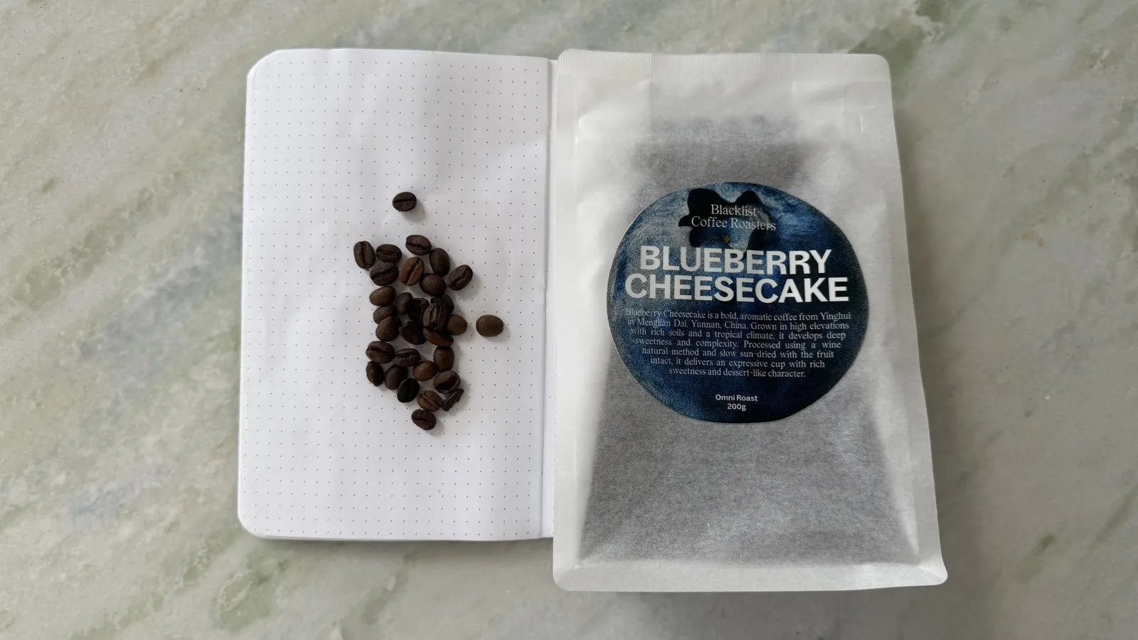 Freshly roasted blueberry cheesecake-flavored coffee beans on white paper with packaging, ideal for coffee enthusiasts and gourmet food lovers.