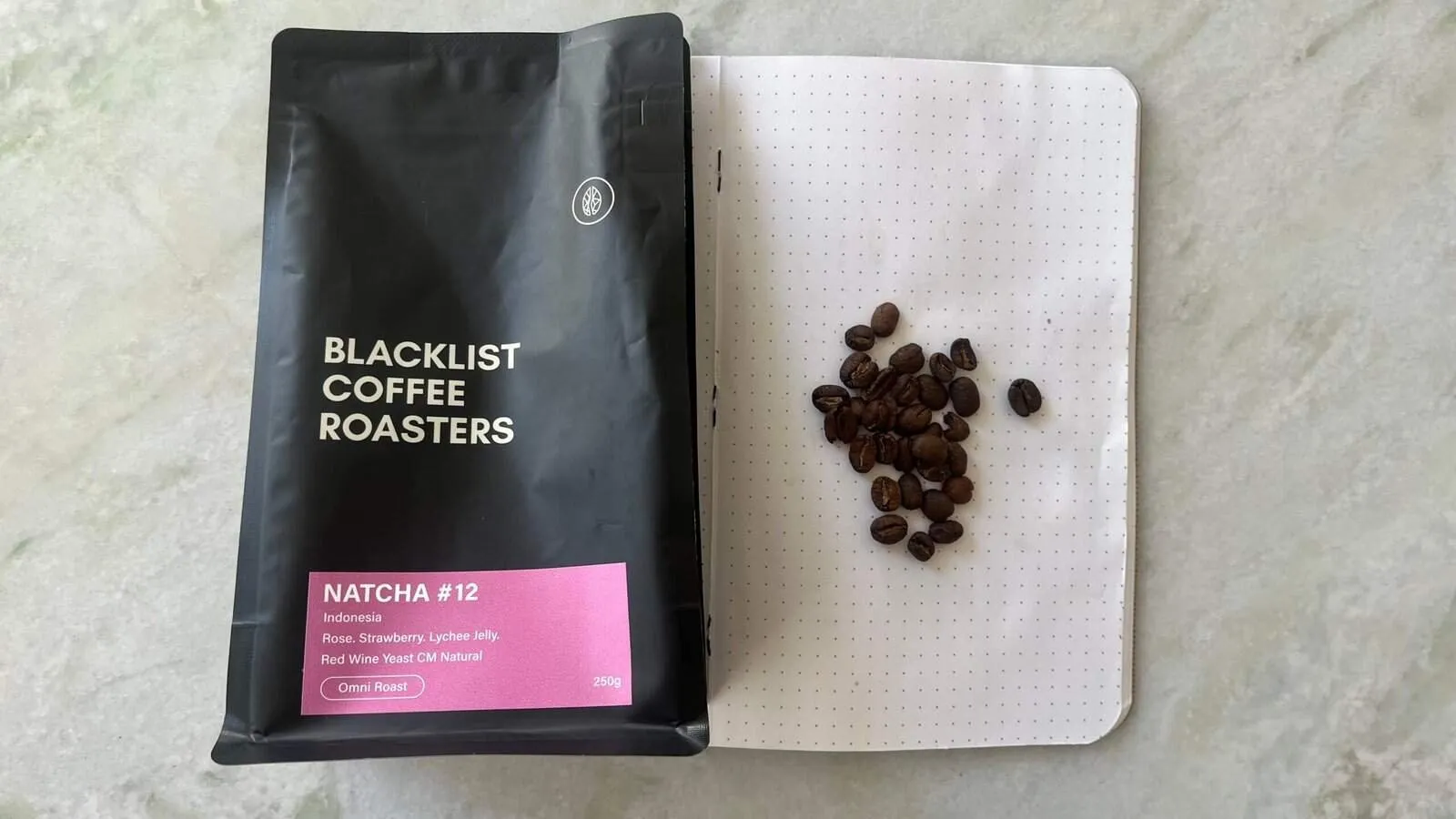 Rich black coffee beans on dotted notebook page with black coffee roast packaging for expert coffee roasting.