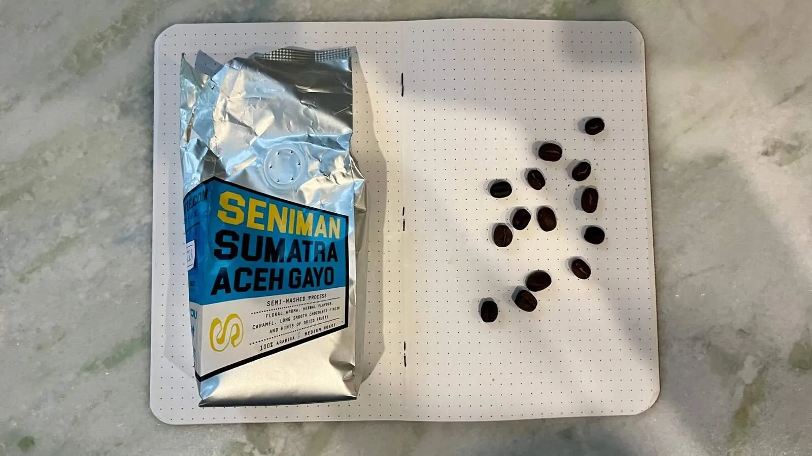Coffee beans displayed on a perforated surface alongside a bag of Sumatra Gayo coffee for making fresh brews.