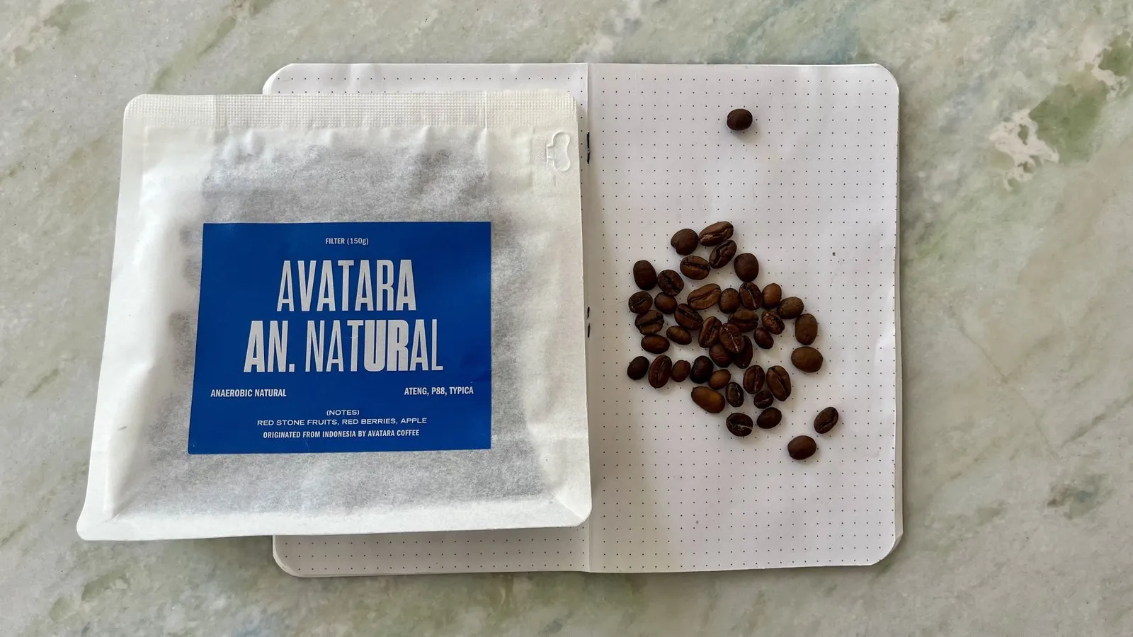 Open coffee sample pack labeled 'AVATARA AN. NATURAL' with roasted coffee beans on a white tray.
