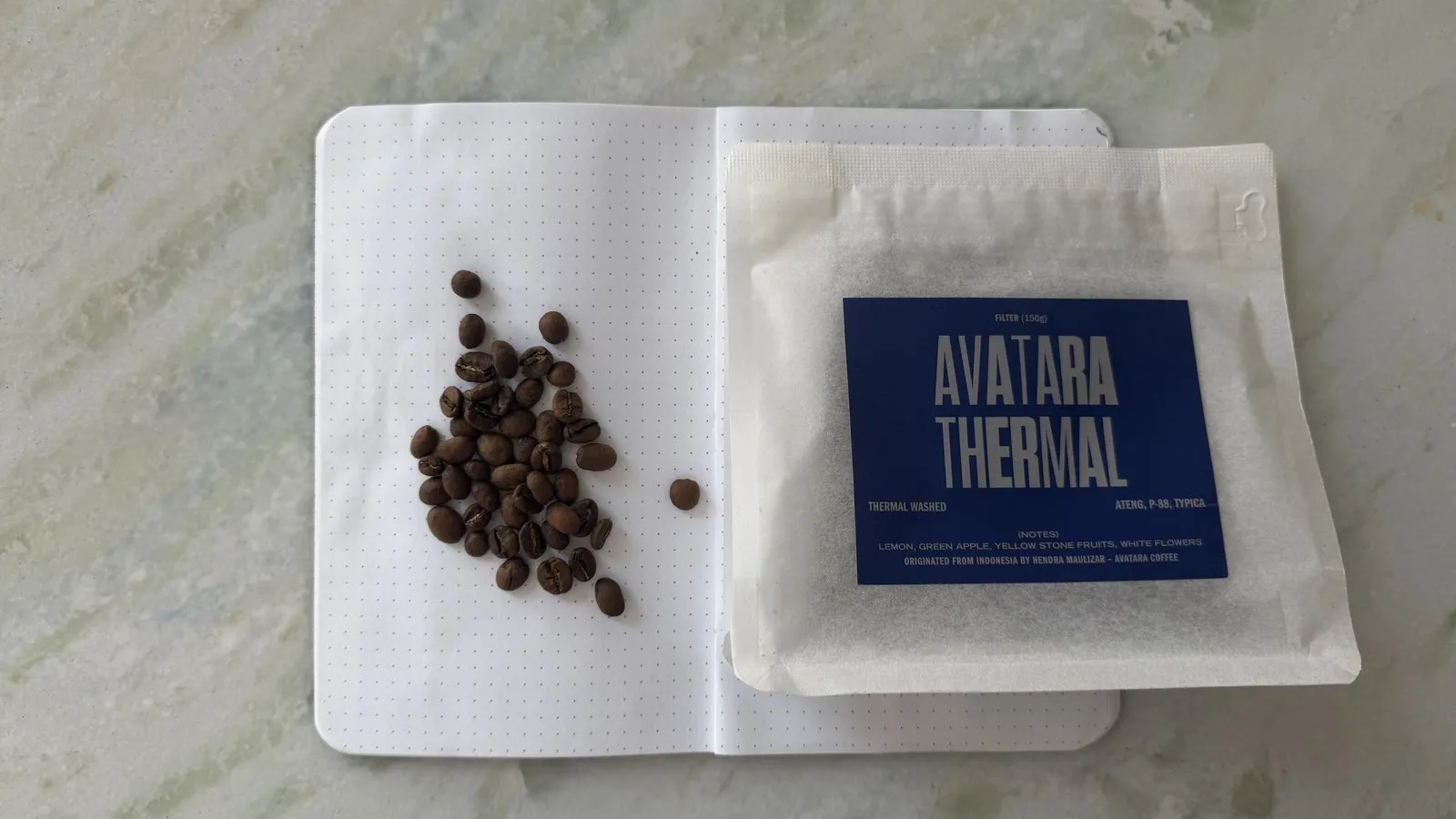 Close-up of Avatar Thermal coffee packets and coffee beans on a white surface, showcasing the product and ingredients.