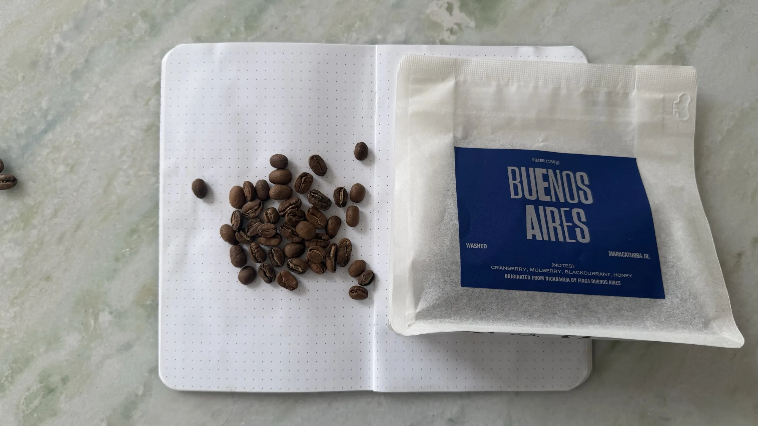Two Hands Full Buenos Aires coffee bag and roasted beans on a dotted notebook.
