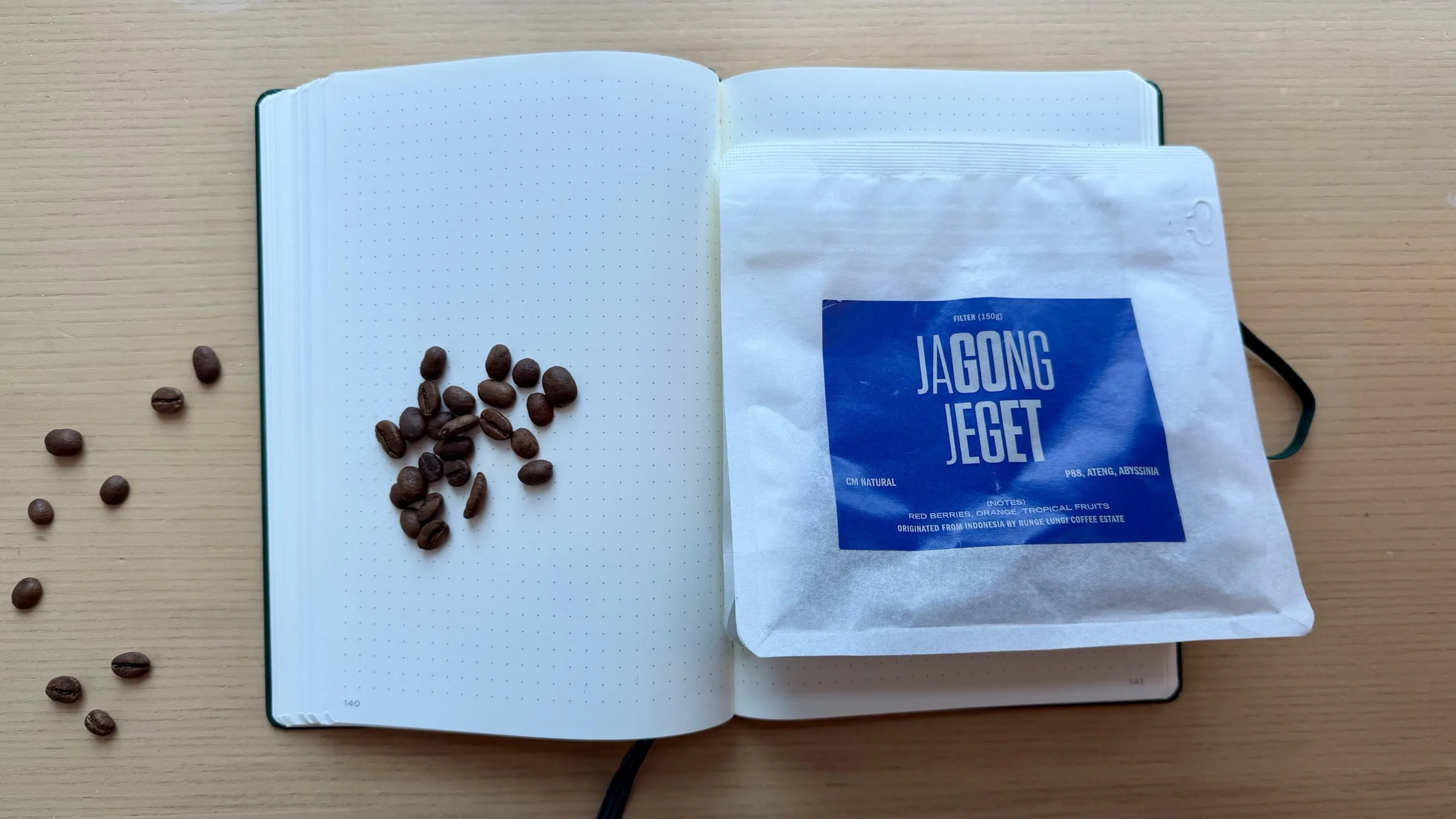 Two Hands Full Jagong Jeget coffee bag beside roasted beans on a dotted notebook page