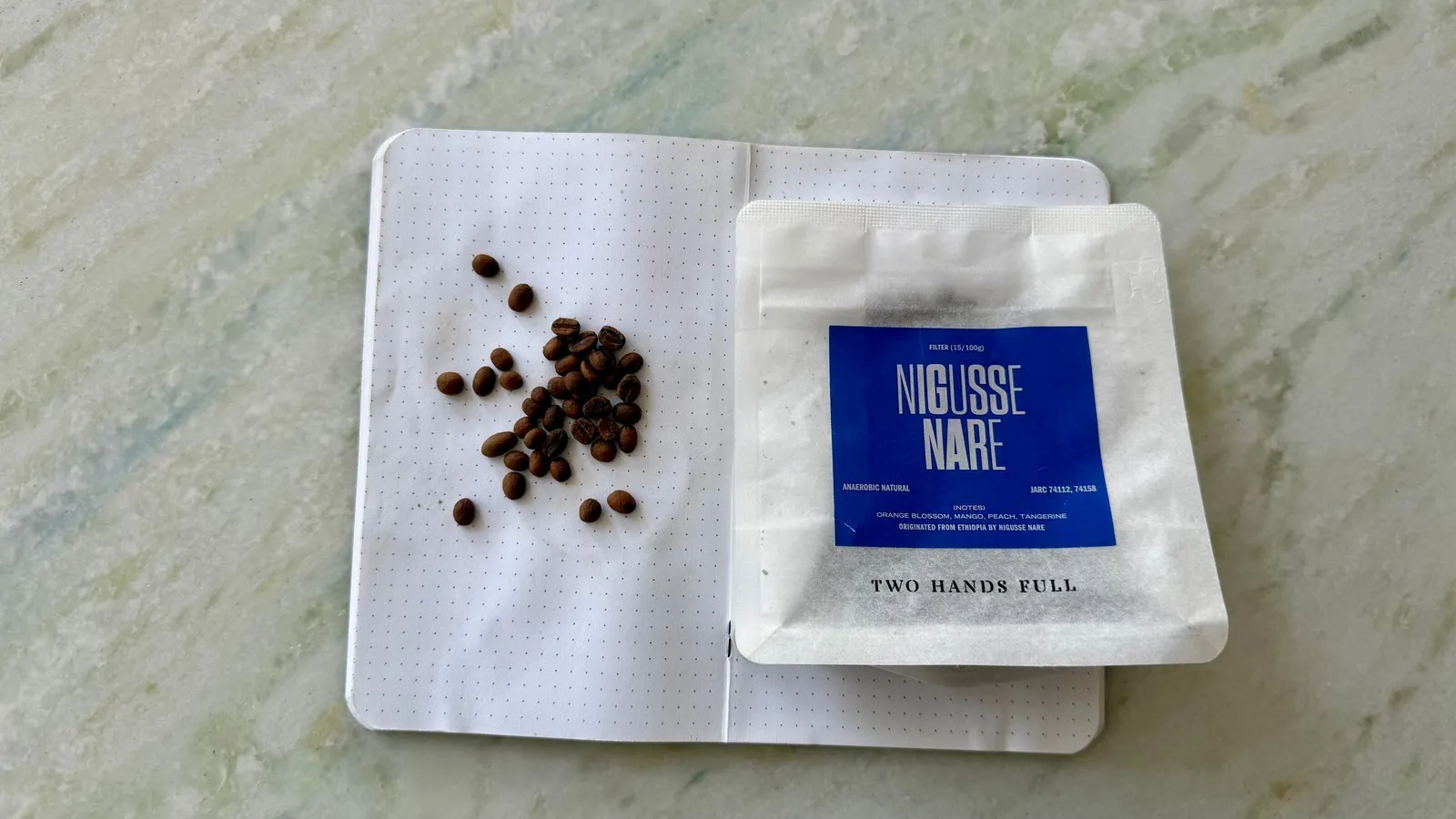 Roasted coffee beans and a "NIGUSSE NARE" coffee bag on an open notebook.